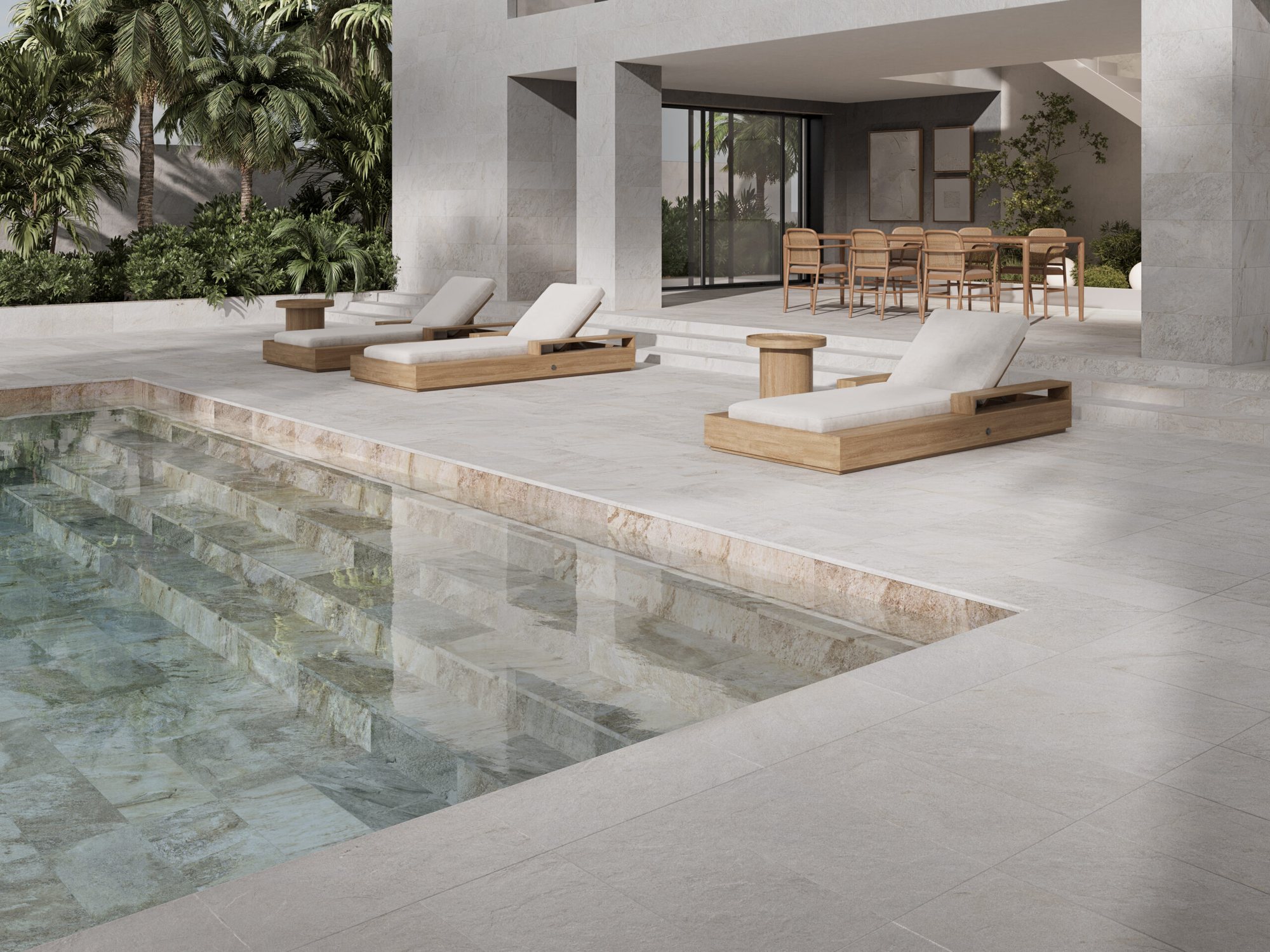 Poolside terrace in pale stone-effect tiles, with sun loungers and a shaded outdoor dining area