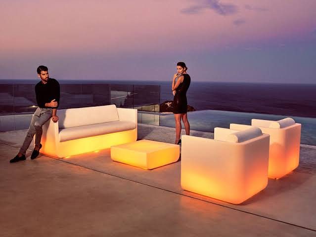 Illuminated outdoor sofa and cubes glowing at dusk on a terrace overlooking the sea