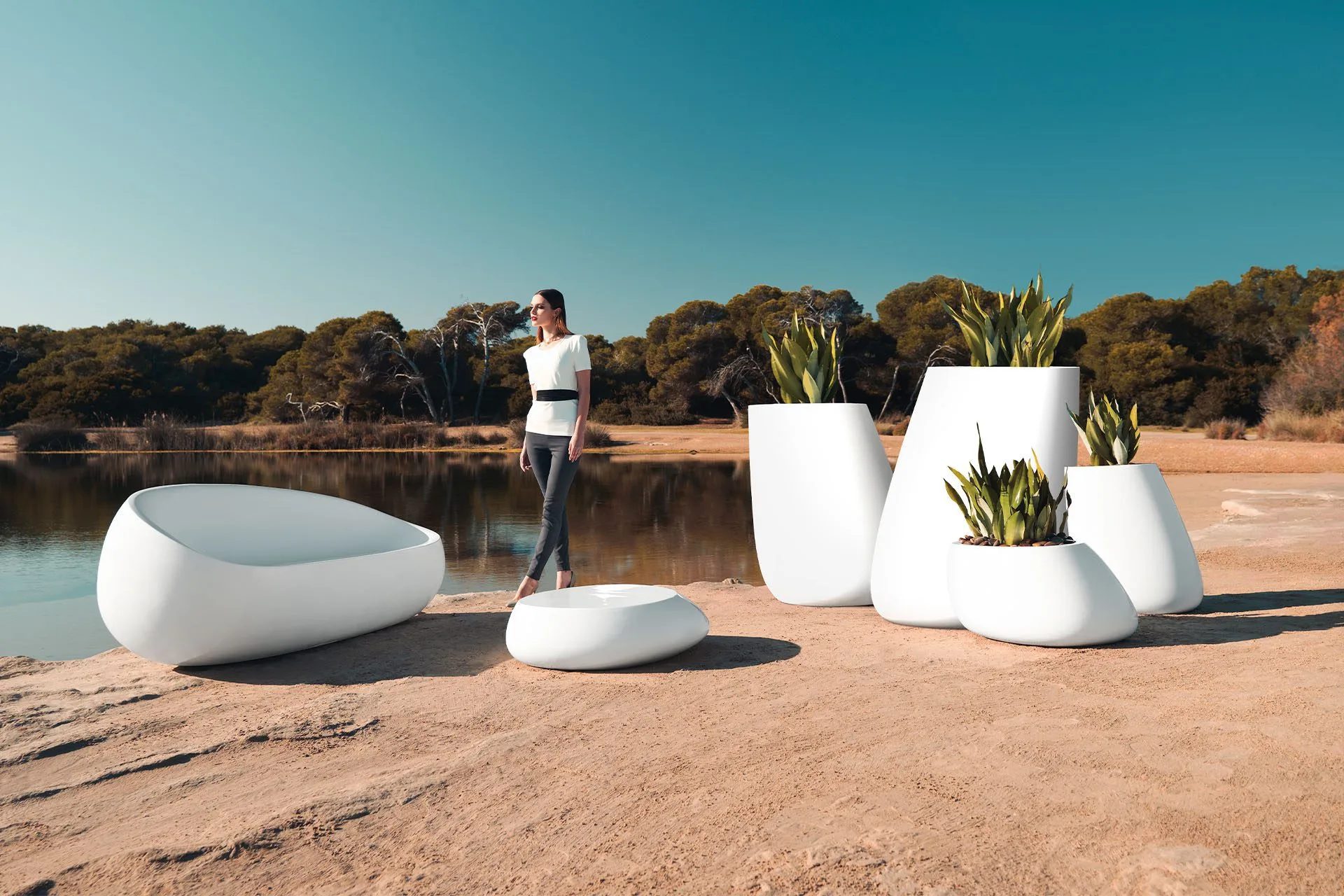 Sculptural white outdoor seat and agave planters on a lakeside beach