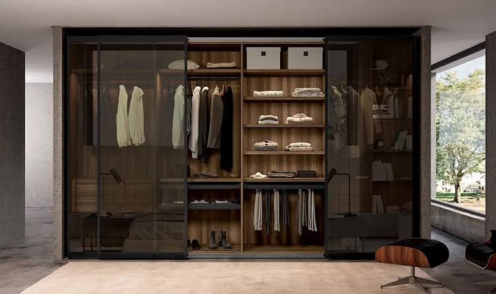 Walk-in wardrobe behind glass sliding doors, with open shelving and hanging rails