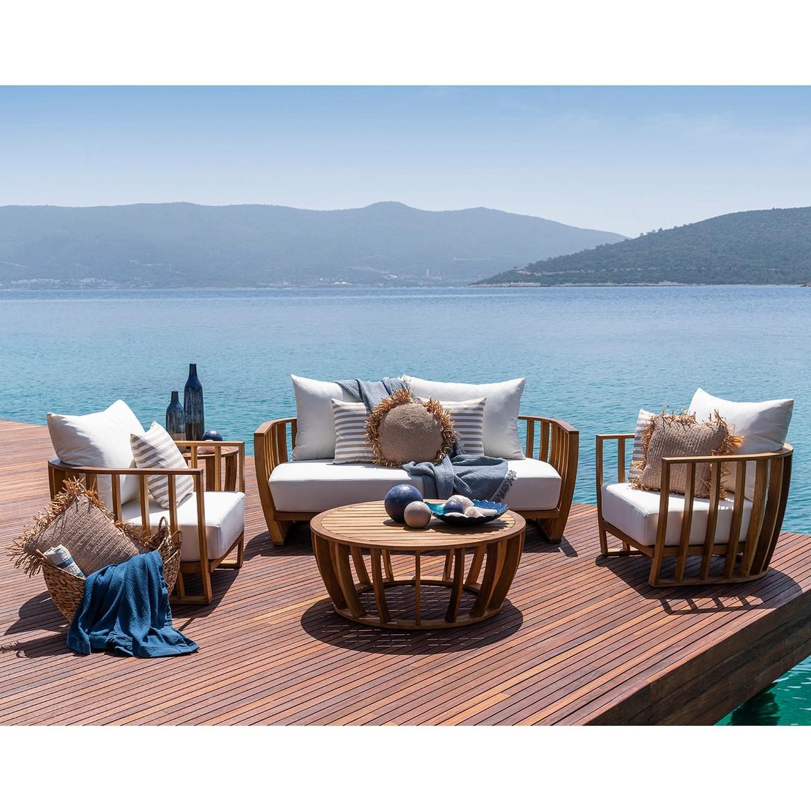 Teak outdoor sofa and armchairs on a timber deck above the sea
