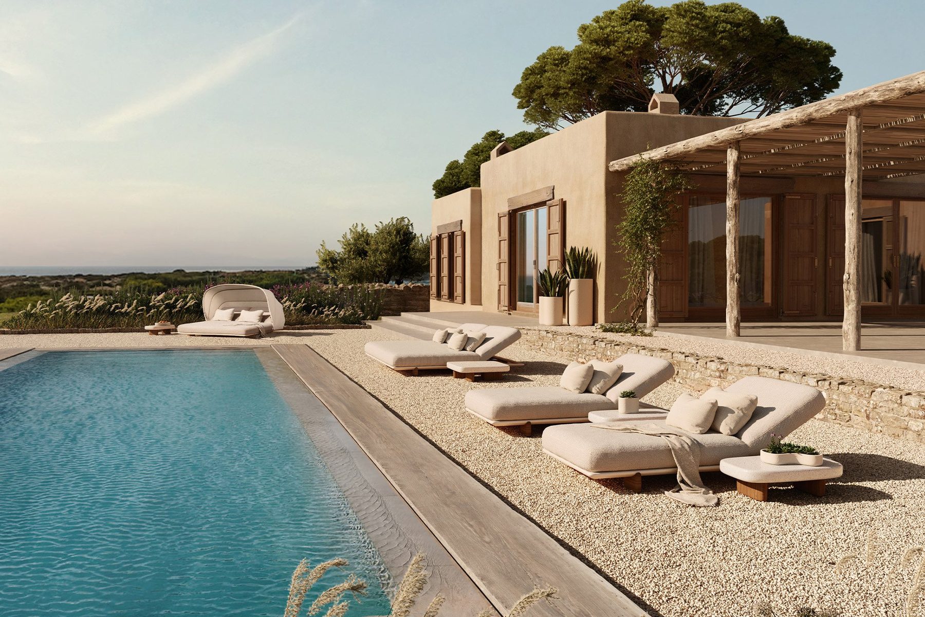 Sun loungers and a daybed along a long pool beside a stone villa on the coast