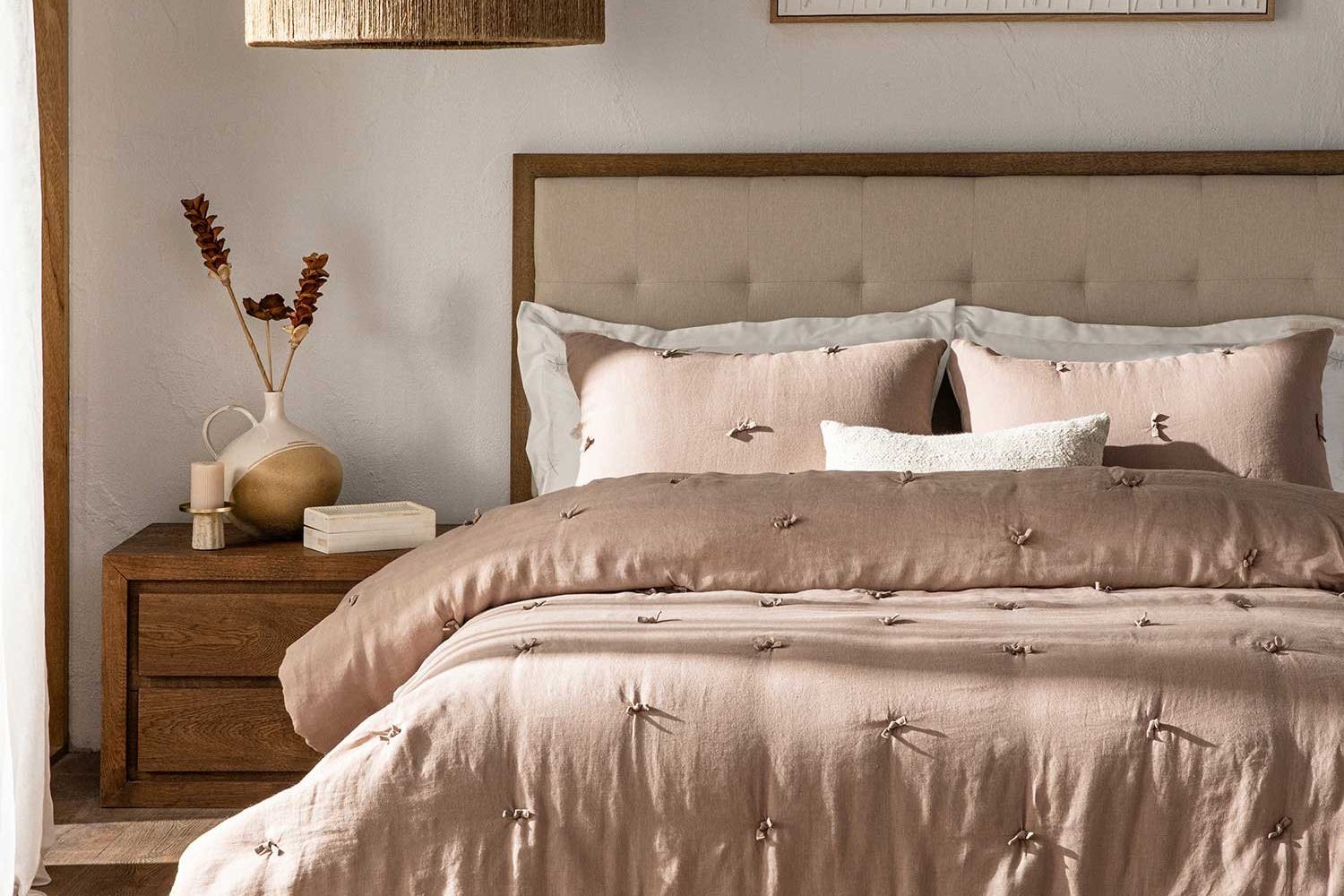 Bedroom with a blush quilted bedspread and cushions against an upholstered headboard