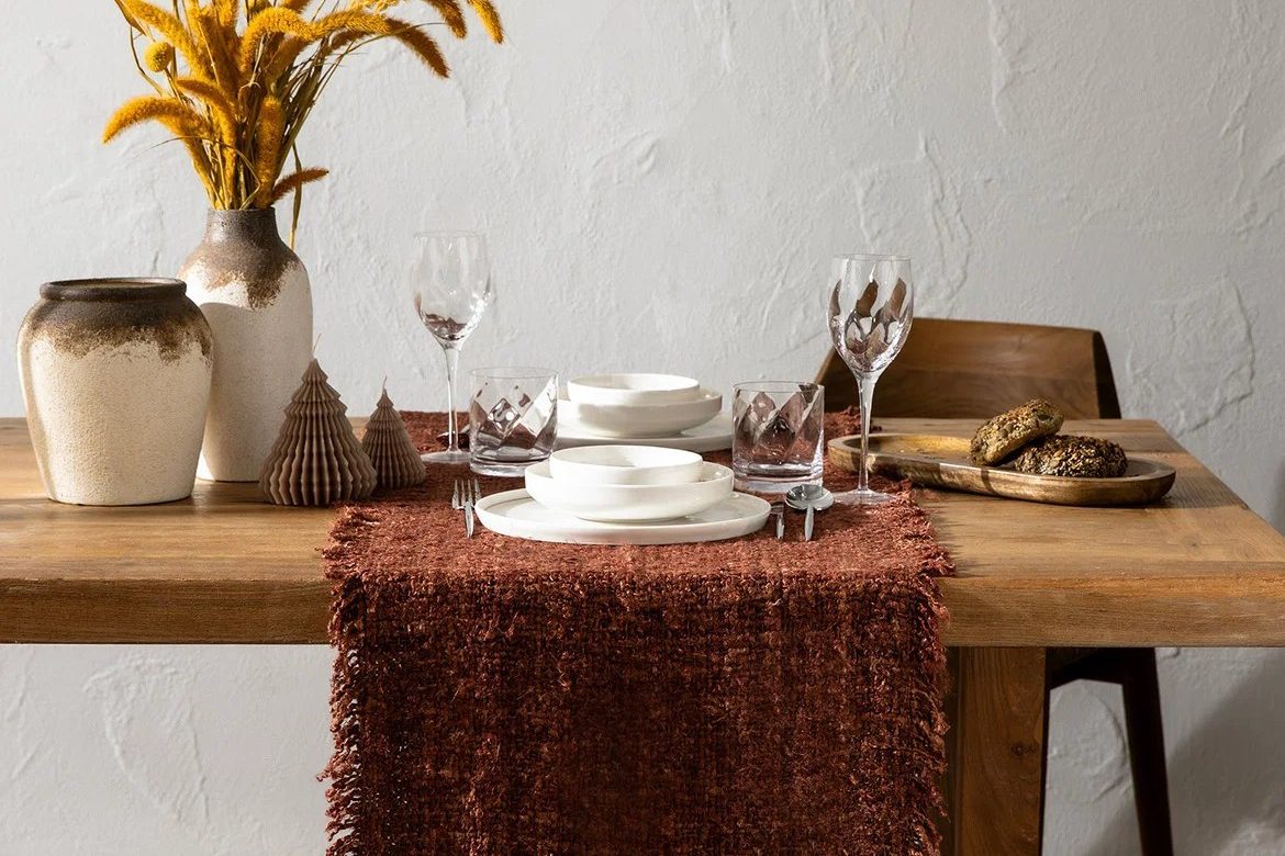 Table set with a rust woven runner, white dinnerware, glassware and dried grasses